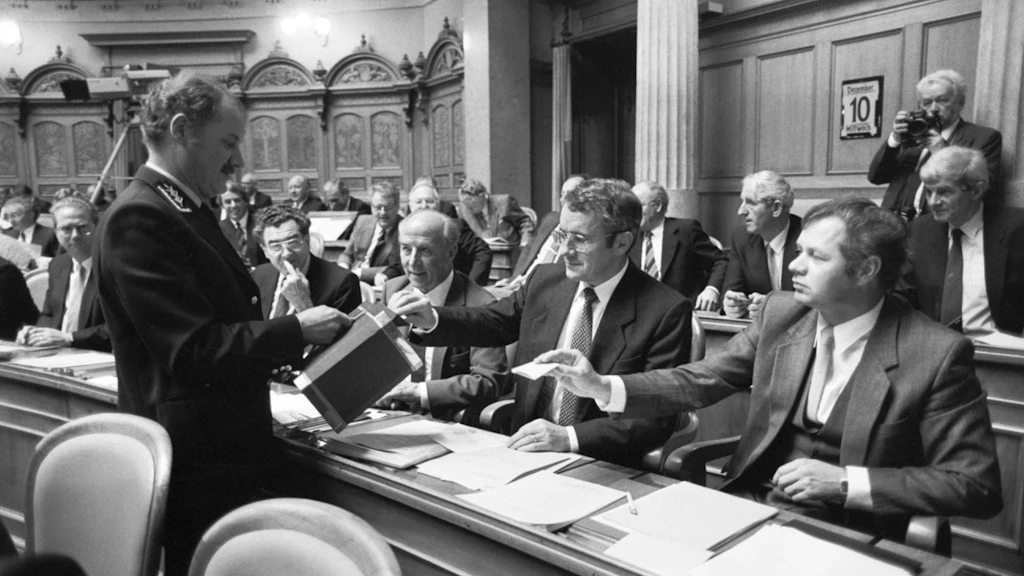 Alt-Bundesrat Arnold Koller gibt in einem schwarz-weiss Bild seine Stimme in der Bundesversammlung ab. Die Szene zeigt den Moment vor seiner Wahl in den Bundesrat; ein uniformierter Beamter hält die Urne, während Koller und weitere Parlamentsmitglieder ihre Stimmzettel einwerfen.