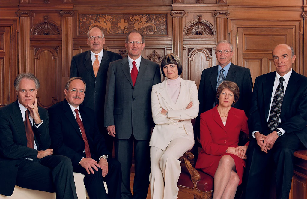 Le Conseil fédéral 2004 in corpore (de gauche à droite): le conseiller fédéral Moritz Leuenberger, le conseiller fédéral Samuel Schmid, le conseiller fédéral Pascal Couchepin, le président de la Confédération Joseph Deiss, la conseillère fédérale Micheline Calmy-Rey, le conseiller fédéral Christoph Blocher, la chancelière de la Confédération Annemarie Huber-Hotz, le conseiller fédéral Hans-Rudolf Merz