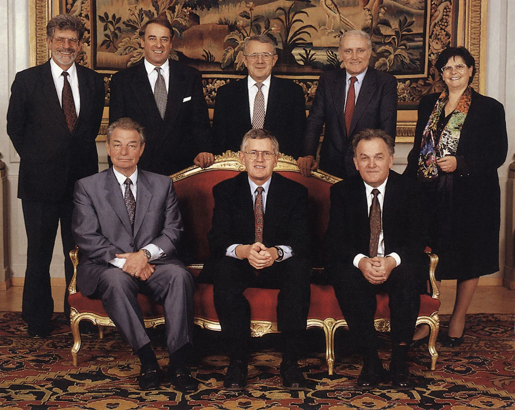 Il Cussegl federal in corpore (da sanester): il chancelier federal François Couchepin, il cusseglier federal Jean-Pascal Delamuraz, il cusseglier federal Adolf Ogi, il president da la Confederaziun Kaspar Villiger, il cusseglier federal Arnold Koller, il cusseglier federal Flavio Cotti, il cusseglier federal Otto Stich, la cussegliera federala Ruth Dreifuss